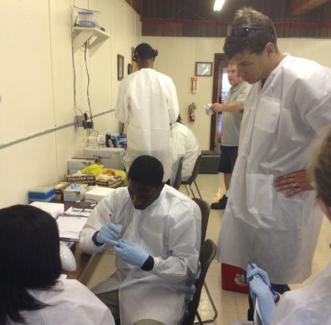 A college professor and high school students in lab coats tracking an experiment