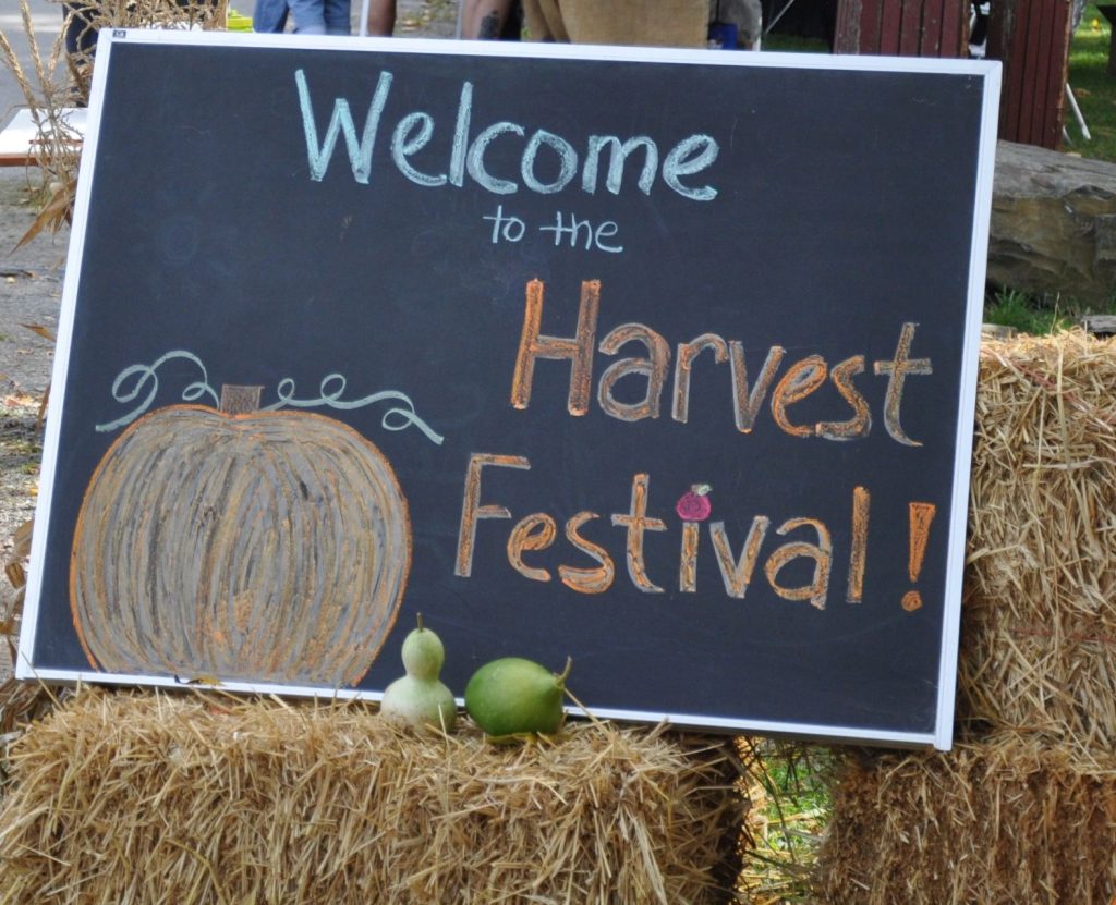 A chalkboard sign resting on hay bales reading Welcome to the Harvest Festival