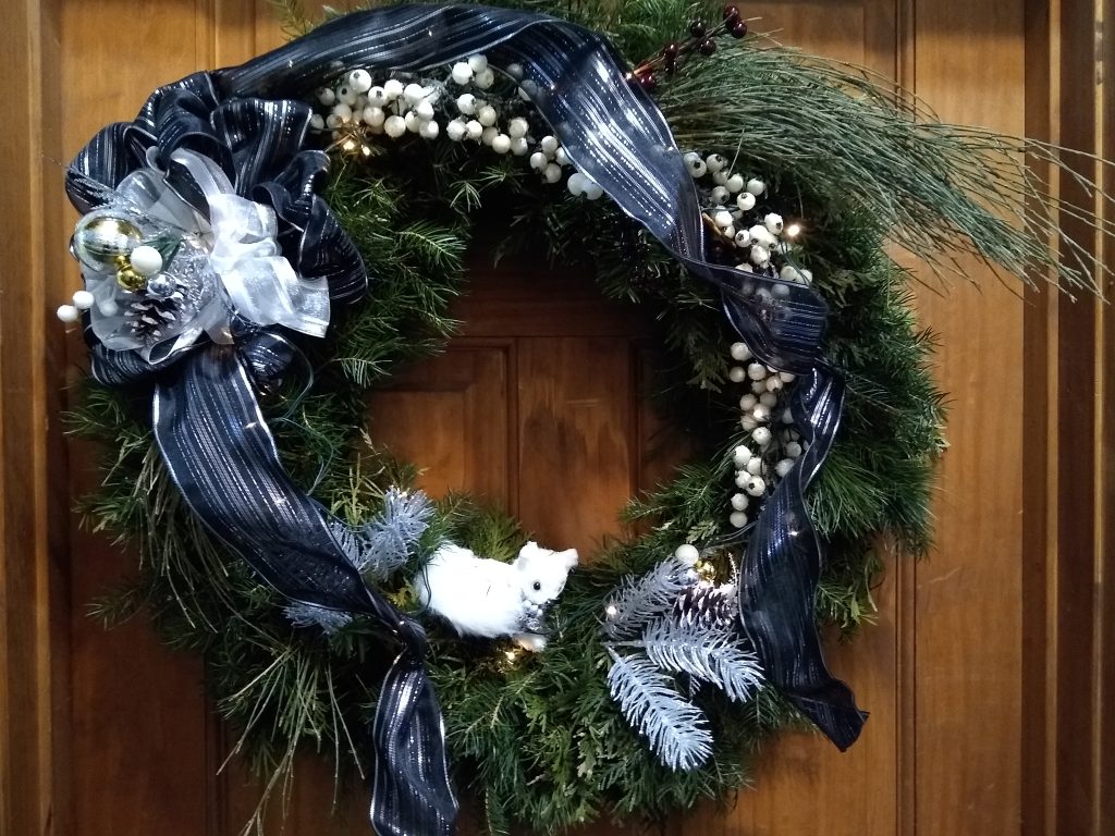 A holiday pine bough wreath with blue and silver ribbon hanging on a door