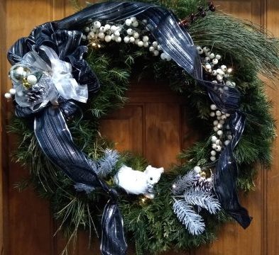 A holiday pine bough wreath with blue and silver ribbon hanging on a door