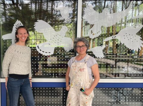 PEEC CEO Amanda Subjin and mural artist Euhri Jones in front of glass windows covered with translucent bird silhouettes