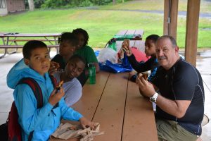 A group of students and a chaperone at a picnic table in a large pavilion